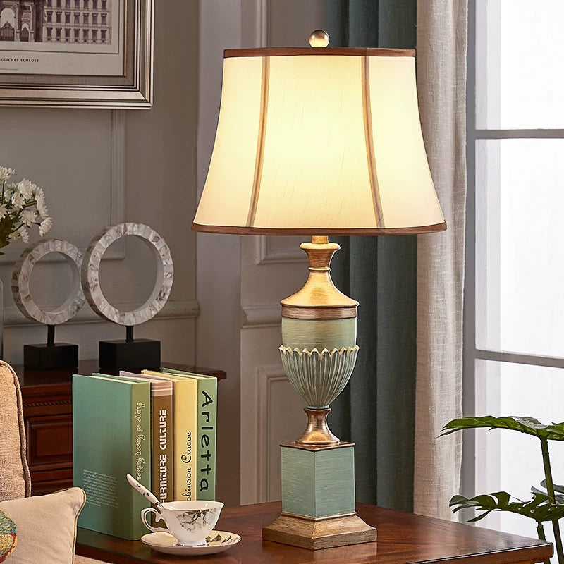 Sage green and antique-gold lamp displayed on a wooden side table.