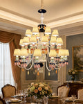 Belle Époque 36-light three-tier chandelier with ivory shades and pastel ornaments above a formal dining table.