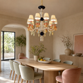 A multi-light chandelier with cream shades and orange, yellow, and white decorative accents hangs over a wooden dining table in a warm, modern dining room with blush pink chairs.