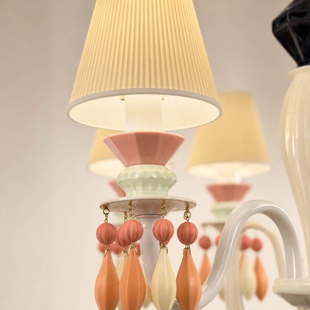 A close-up of a decorative table lamp with pleated cream fabric shades, a white curved arm, pastel pink and mint green accents, and dangling peach and cream teardrop beads.