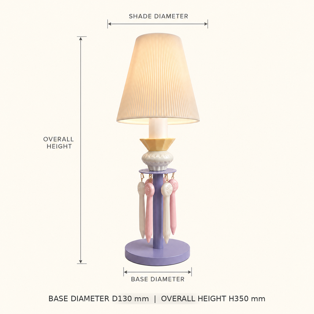 A table lamp with a pleated beige shade, lavender base, and pastel pink and cream hanging tassels, shown with dimension labels for shade diameter, overall height, and base diameter on a light beige background.